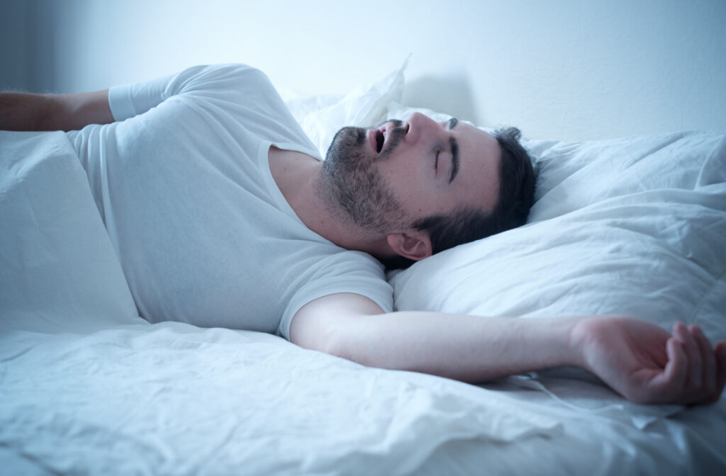 A man sleeping on his back in bed with his mouth open and snoring.
