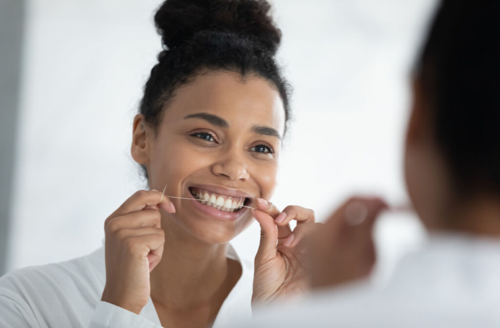 A young woman looking in the mirror and flossing while smiling.