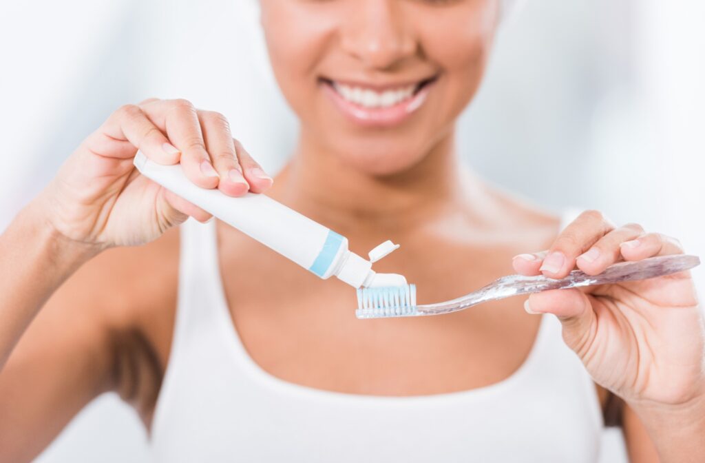A woman smiling and applying a toothpaste on a toothbrush