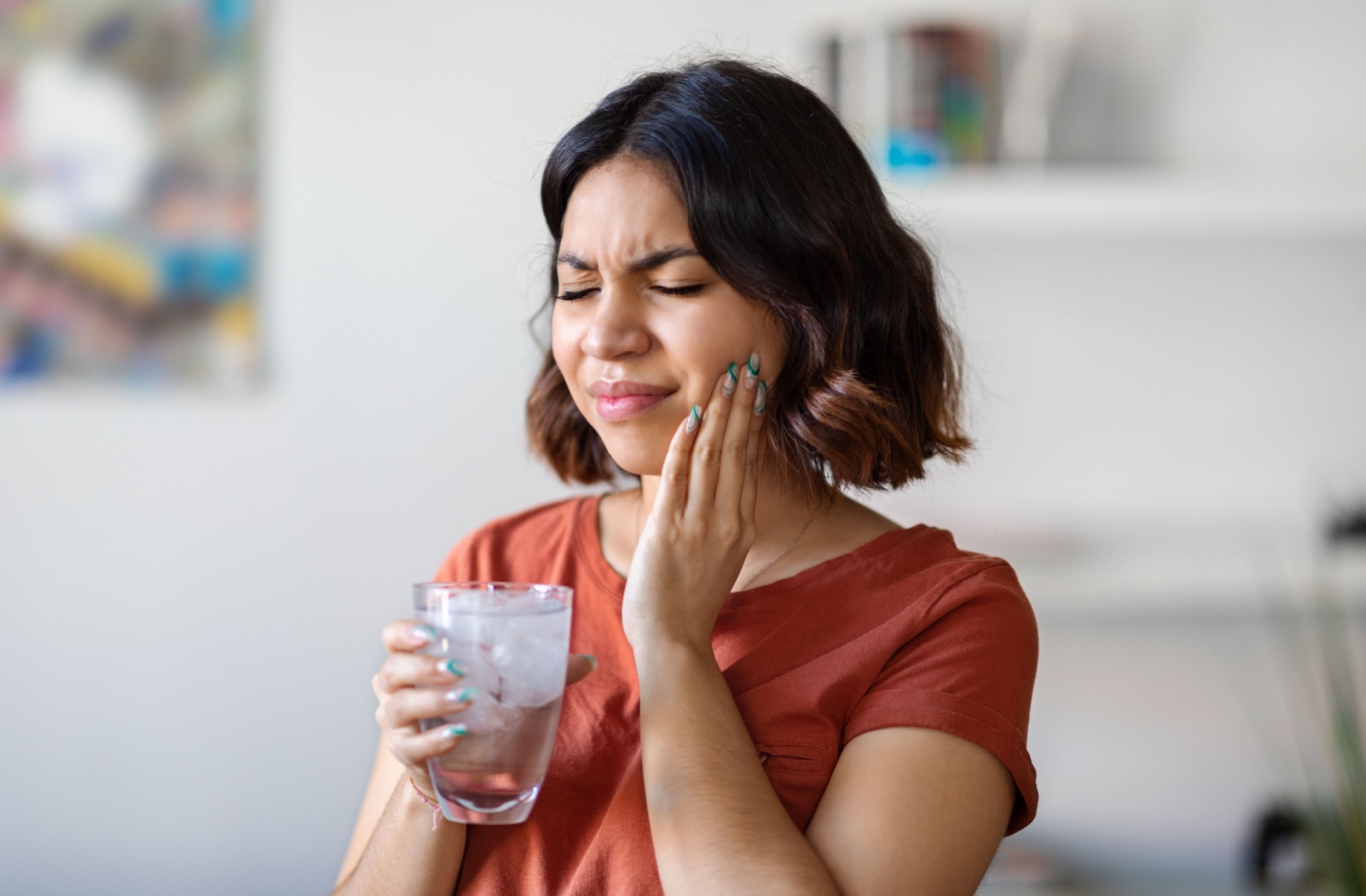 A young woman holding her jaw and drinking a cup of ice water is experiencing tooth sensitivity as a result of weakened enamel.